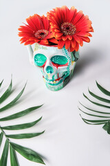 skull with coral color gerbera flowers and palm leaves on white background. Creative concept. Surreal feel, eery spooky atmosphere.