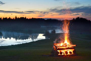 Midsummer national traditional celebration fire flames in the fireplace on grass field near river...