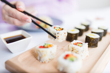 Woman hand taking piece of sushi roll with chopsticks. Healthy seafood asian japanese dish.