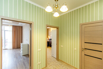 The corridor in the apartment, the doors open to different rooms. Light green Wallpaper with white stripes