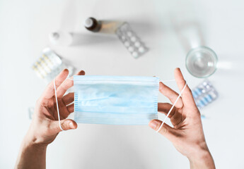 Male hands holding a surgical mask on the background of a table with pills medicines and medications for treatment.