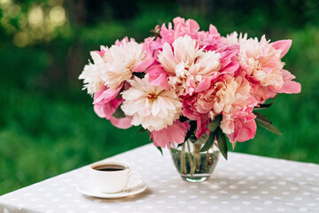 A cozy romantic breakfast in the open air. A vase of peonies flowers, a cup of coffee tea on the table. Soft selective focus.