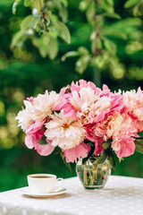 A cozy romantic breakfast in the open air. A vase of peonies flowers, a cup of coffee tea on the table. 