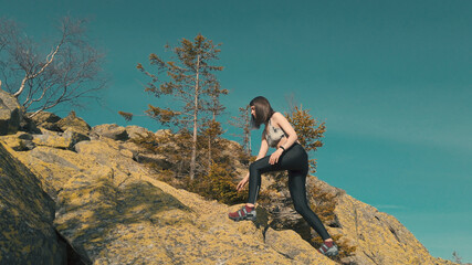Beautiful athletic woman scrambling on a peak of a mountain. Female enjoys active leisure. looking into the distance