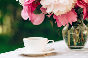 Fototapeta na wymiar A cozy romantic breakfast in the open air. A vase of peonies flowers, a cup of coffee tea on the table. 