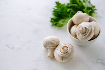 Champignon mushrooms in a white bowl with herbs on the table close-up.