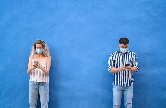 Young people wearing surgical mask using mobile phone keeping social distance - Millennial friends watching media trends on smartphones during corona virus outbreak - Youth and technology concept