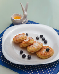 Syrniki or cottage cheese pancakes with blueberries and honey on white plate with blue napkin on kitchen table. Healthy breakfast, diet concept.