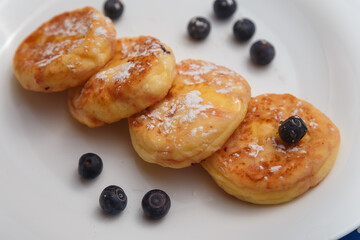 Traditional syrniki or cottage cheese pancakes with blueberries on white plate with blue napkin on kitchen table, close up.