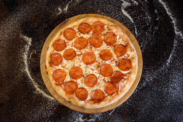 Top view of pepperoni pizza on the black background with spilled flour. Restaurant menu presentation.