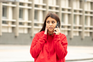 Beautiful surprised dark-skinned woman carefully listens to the interlocutor on the smartphone while walking along the street