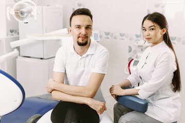 Dentist and assistant are sitting in the office and looking at the camera