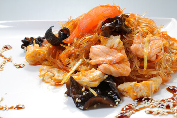 Rice noodles with salmon, wood mushrooms and tomatoes on a white plate