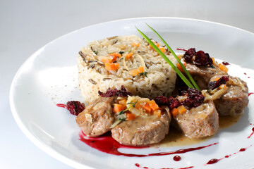 Meat medallions with wild rice and vegetables in a cranberry sauce on a white plate