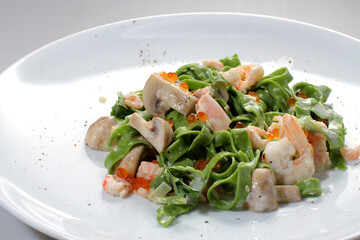 Green noodles with spinach, shrimp, caviar and mushrooms on a white plate