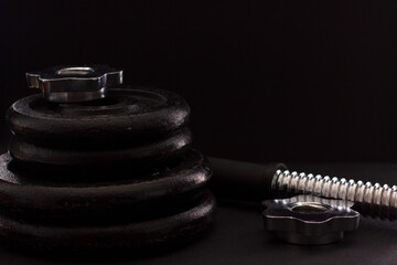 Black metal dumbbell for fitness with a chrome handle, on a black background.