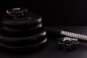 Black metal dumbbell for fitness with a chrome handle, on a black background.