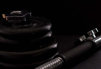 Black metal dumbbell for fitness with a chrome handle, on a black background.