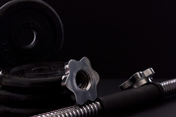 Black metal dumbbell for fitness with a chrome handle, on a black background.