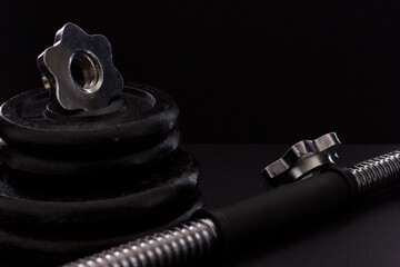 Black metal dumbbell for fitness with a chrome handle, on a black background.