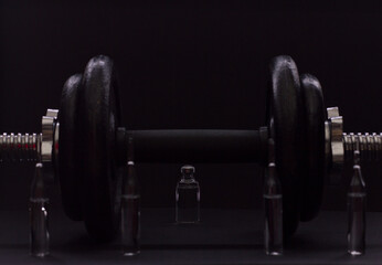 Fototapeta na wymiar Black metal dumbbell for fitness with ampoules, on a black background.