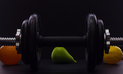 Black metal dumbbell for fitness with fruits, on a black background.