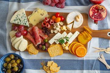 A wooden cutting board full of different types of cheese, bacon, and a few fruits. Overhead view.