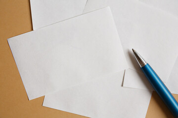 White sheets of paper for notes on a brown paper background and a blue metal pen flat lay