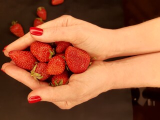 Strawberry in the female hands with red manicure.