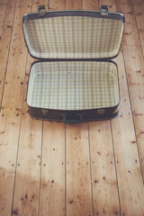 Plakat An open old vintage brown travel suitcase on a wooden floor
