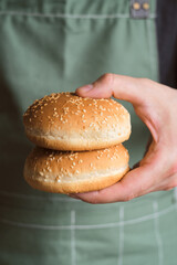 Burger buns in the hands of a man. Baking buns. Cooking hamburger, ingredient for the dish. Chef in an apron. Beautiful fresh buns with sesame seeds close-up. Traditional american delicious lunch