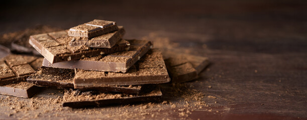 Bars of dark chocolate and cocoa on brown wooden background. Close up view
