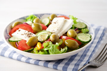 Greek salad with feta cheese, tomatoes, cucumbers, lettuce, olives and spices. Traditional greek cuisine. White rustic wooden table