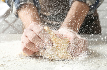 Young man kneading dough at table in kitchen, closeup