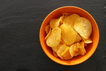 Top view image of potato chips slices in the bowl over slate stone background