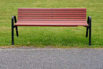 A wooden bench in a park with green grass on a background.