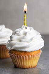 Cupcake with a birthday candle on a gray background.