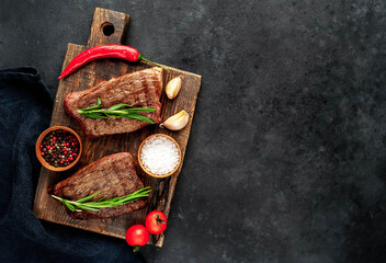 
Two grilled beef steaks with spices on a stone background with copy space for your text.