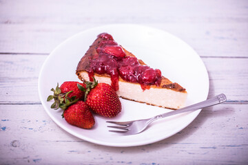 Brownie cheescake with strawberries perfectly arranged on a plate on white wooden table.
