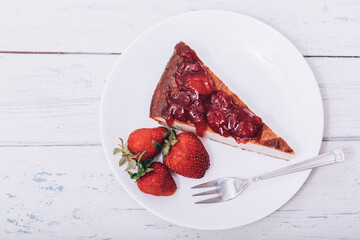 Brownie cheescake with strawberries perfectly arranged on a plate on white wooden table.