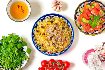 National Uzbek pilaf with meat, achichuk salad of tomato, cucumber, onion in plate with traditional pattern, cilantro, cherry tomatoes, garlicbread tortilla - patir on white wooden table Top view - 356659792