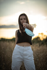 Young woman with black hair wearing a mask for health care in a field at the evening surrounded by...