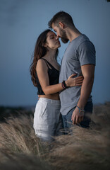 Young couple of man with beard and girl with long dark hair hugging and smiling between plants in the middle of a field in the wild nature