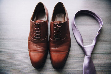 Men's fashion. Brown leather shoes stand on a wooden surface next to a tie.
