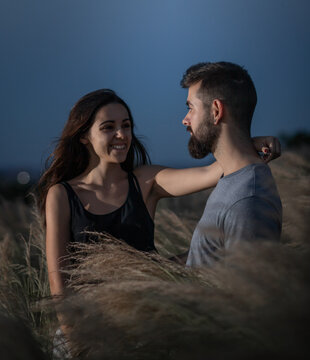 Young couple of man with beard and girl with long dark hair hugging and smiling between plants in the middle of a field in the wild nature