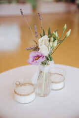 On a table with a white tablecloth is a vase with a composition of flowers and two candles in glass candlesticks