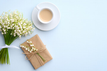 Coffee mug with bouquet of flowers lily of the valley and gift box on blue background. Good morning coffee, happy mother's day concept. Flat lay, top view.