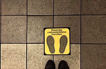 Newyork , usa - 8 June ,2020 : Closeup of feet standing onthe floor with yellow social distance sign - image  