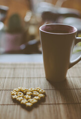 Сup of hot coffee comes from steam, and next to it is a cereal heart for breakfast. Love