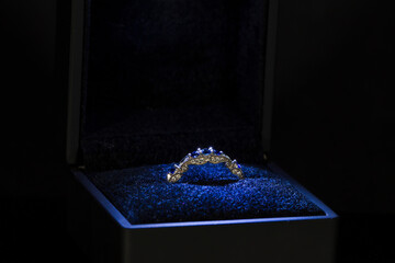 Engagement ring with blue stones in blue light in a box.